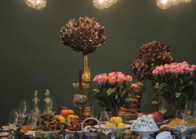 A luxurious dining setting with an opulent centerpiece. There are two large floral arrangements, one on a tall gold stand and the other directly on the table, both consisting of densely packed dark and light pink flower