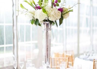 Modern floral arrangement centerpiece with white, green, and purple flowers in a silver vase, ideal for weddings and social events.