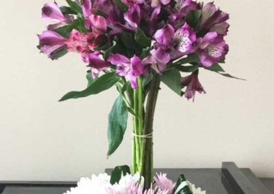 A bouquet of flowers with predominantly purple petals and some green foliage, placed in a clear glass vase. The flowers appear to be fresh and vibrant, which could indicate a recent acquisition or that they are well-maintained