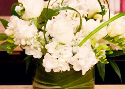 A floral arrangement consisting of white flowers, which include roses and other varieties, with green leaves and stems.
