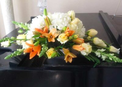 Modern floral arrangement with white, orange, and yellow flowers on a piano; perfect for weddings, corporate events, or social occasions in Orange County.