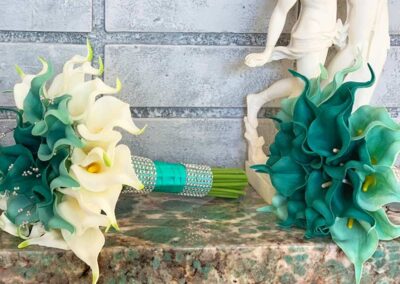 Two bouquets of calla lilies, one with white flowers and the other with teal flowers, both tied with a matching ribbon.