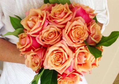 A person holding a bouquet of roses. The bouquet consists of several large, blooming roses with petals ranging in color from creamy peach to vibrant pink.