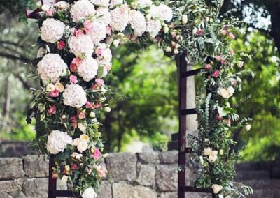 a beautifully adorned floral archway, primarily decorated with large blooming pink and white roses, complemented by smaller flowers and lush green foliage.