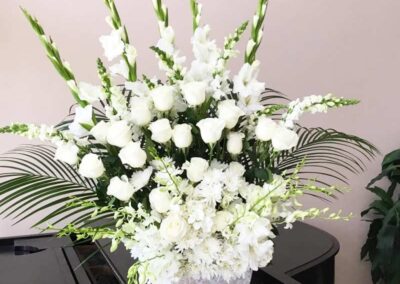 A beautiful and sophisticated floral arrangement consisting of white flowers, including roses and gladiolus, complemented by green ferns and other foliage.