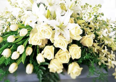 A beautiful floral arrangement featuring a combination of white lilies, yellow roses, and white tulips interspersed with green foliage.