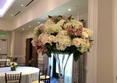 Modern floral arrangement with white roses and pink flowers in tall glass vase for weddings, corporate events, and social gatherings.